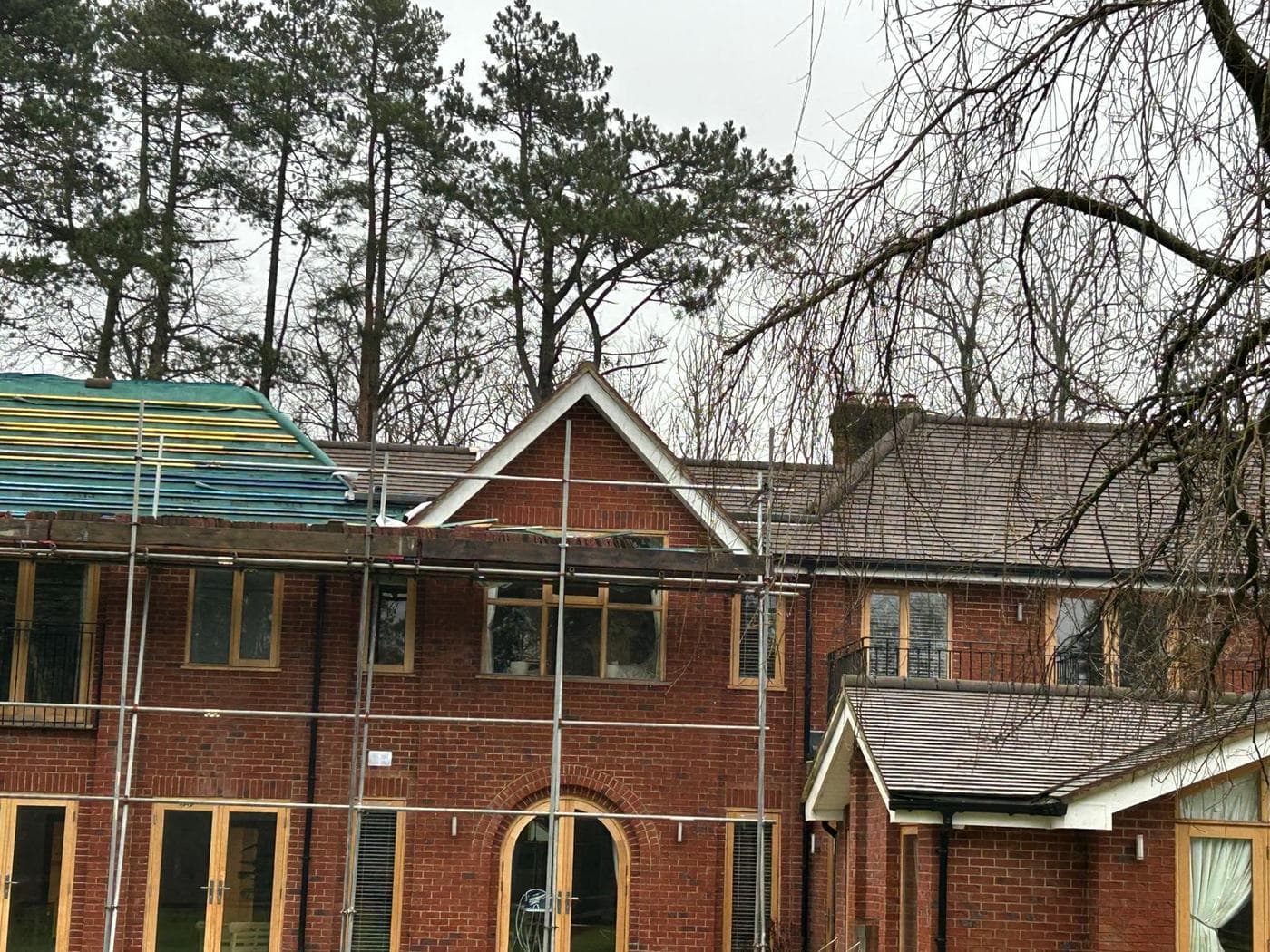 Scaffold around a red brick gable with the roof behind sheeted in blue tarpaulin