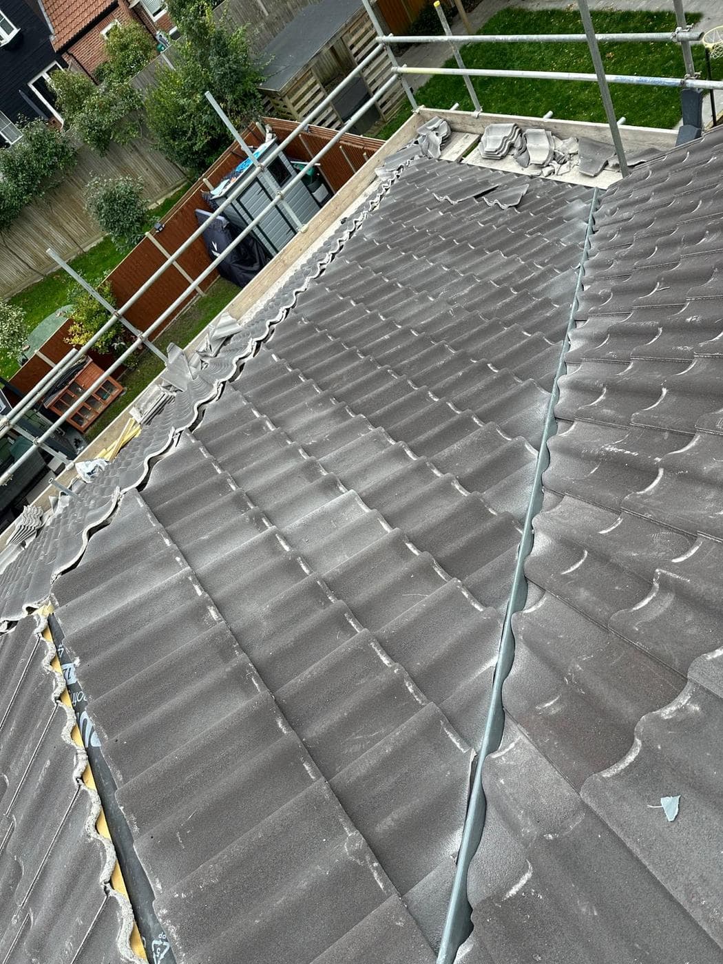 Freshly laid grey interlocking tiles running down two slopes, spare tiles stacked by the ridge
