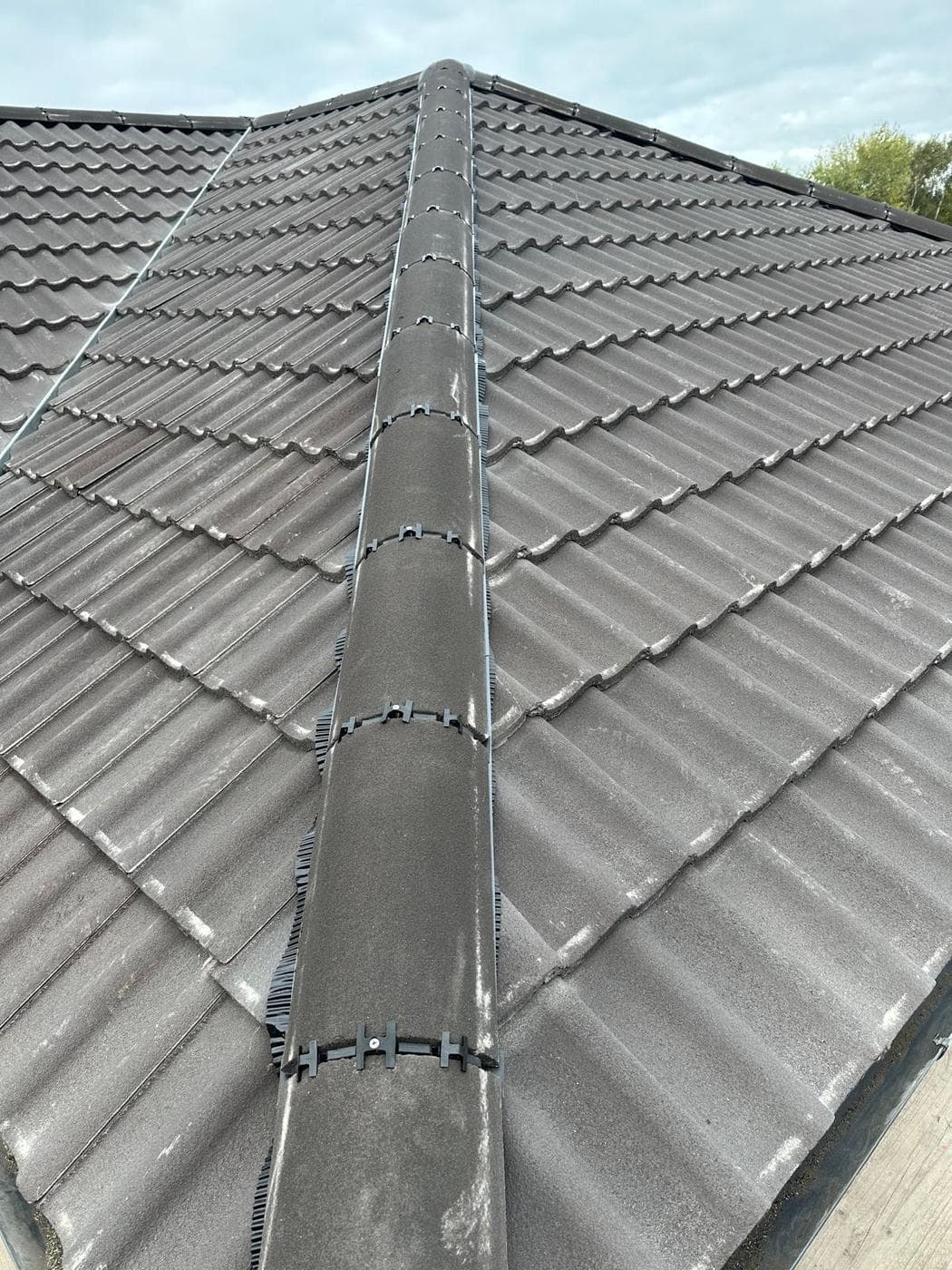 Two grey tiled slopes meeting at a clipped ridge, hip tiles running to the eaves