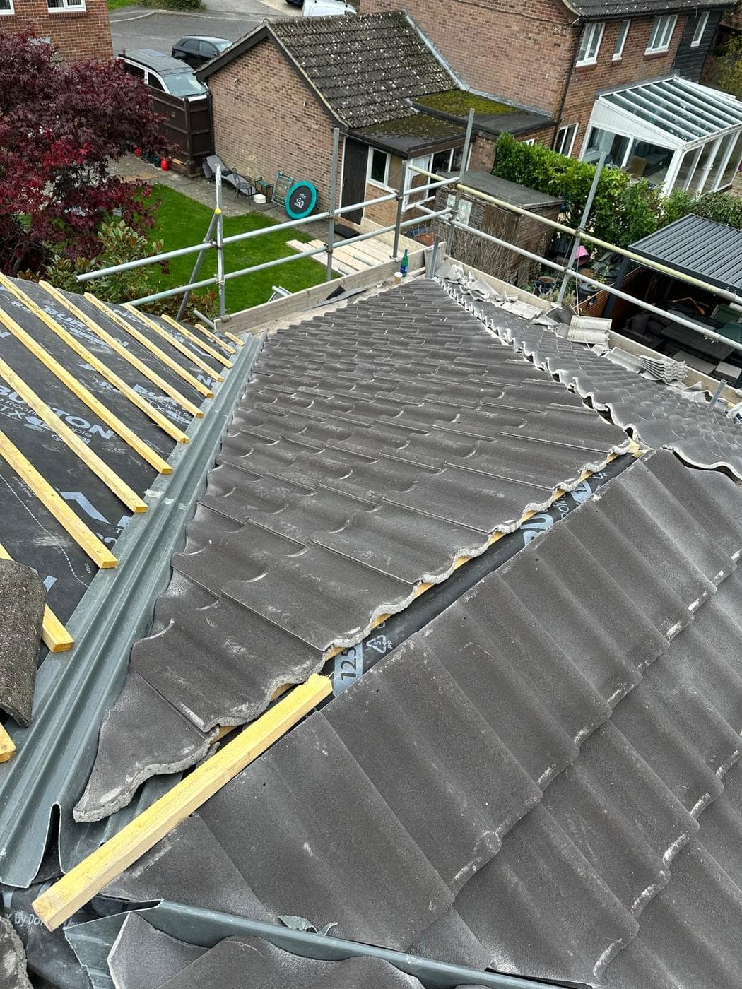 Half-stripped pitched roof, new battens over membrane on one slope, grey tiles laid on the other