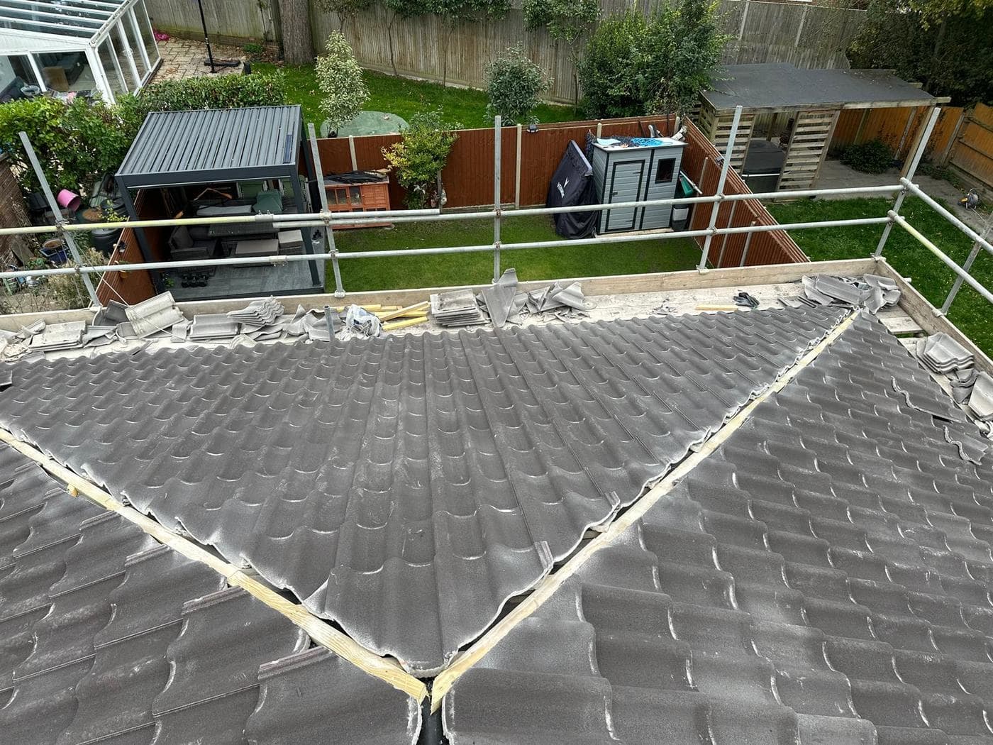 Half of a hipped roof re-tiled, loose tiles waiting at the ridge above a garden