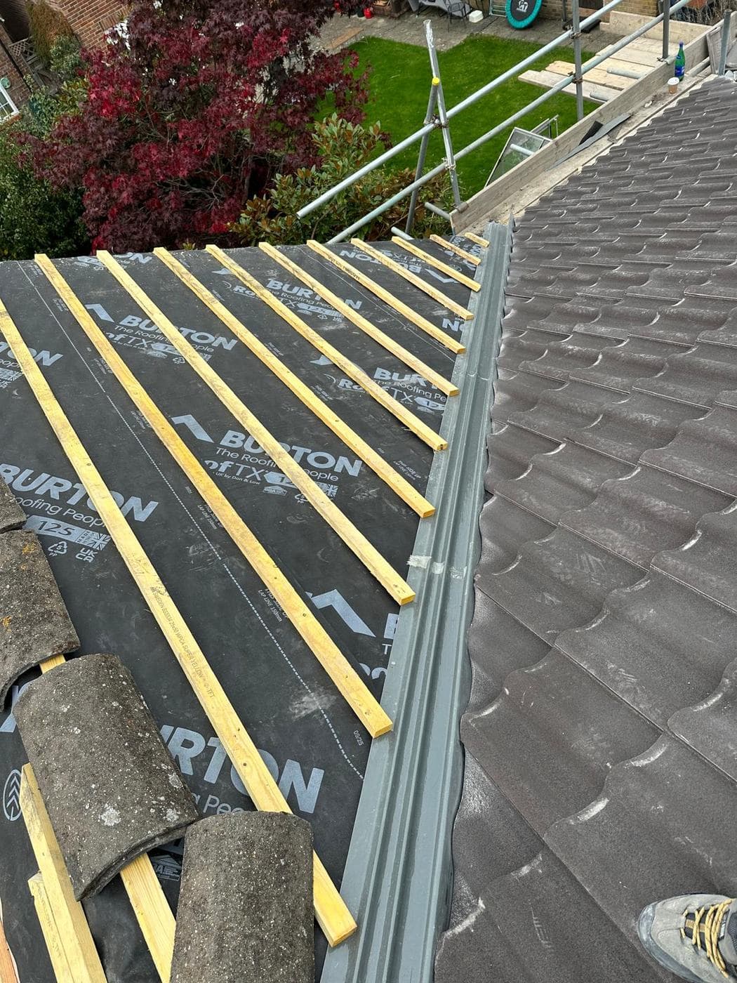 Breathable membrane and fresh timber battens on a stripped slope beside finished tiling