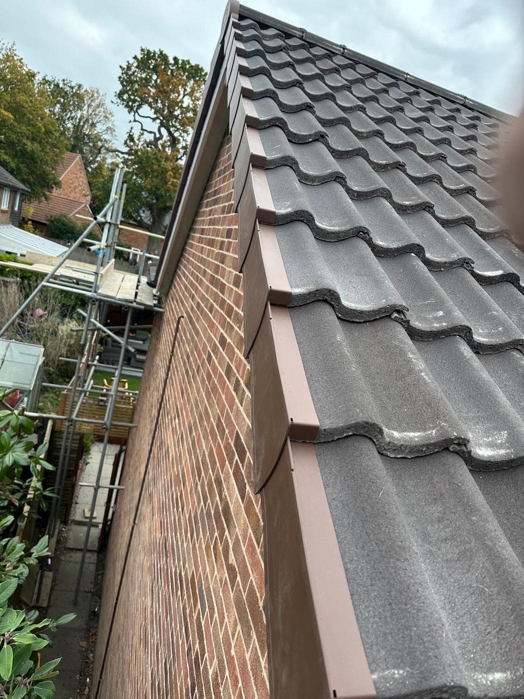 Brown dry verge capping a red brick gable edge, scaffolding and garden below