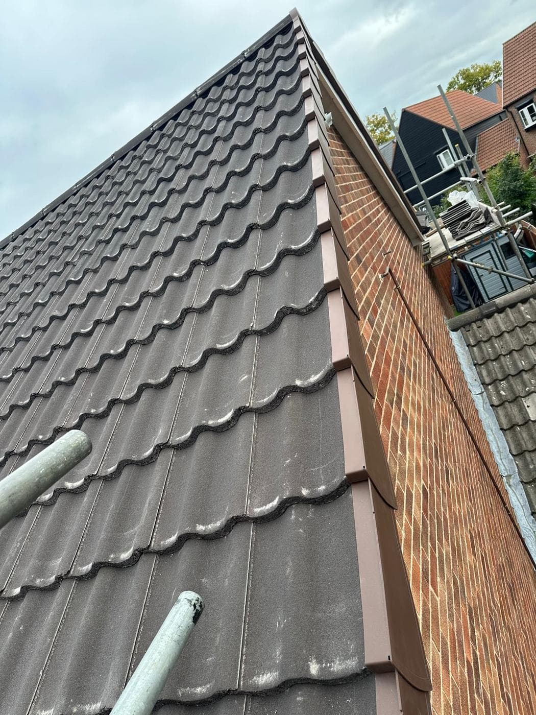 Scaffold poles across new grey roof tiles at a gable, brown verge trim alongside