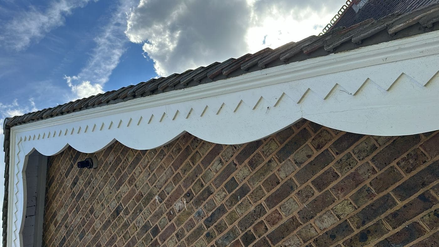 Ornate white bargeboard with dentil detail running the length of a brick gable