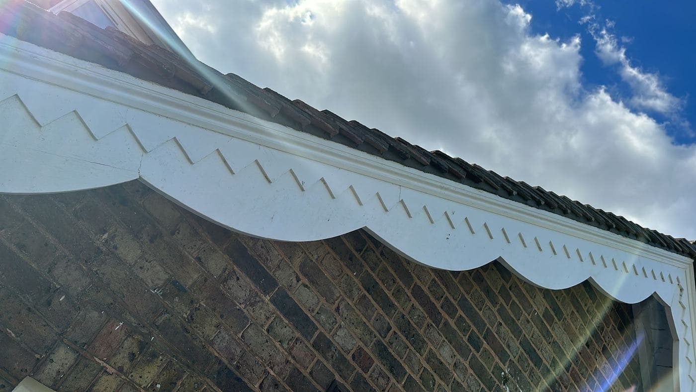 Decorative white scalloped bargeboard below clay tiles on a sunlit stock brick gable