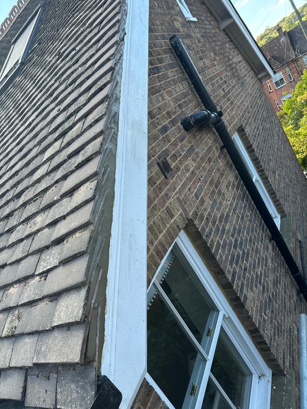 White painted verge board and bedded tiles beside a black downpipe on stock brick