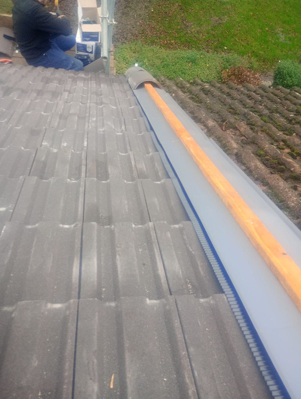 New timber ridge batten and grey dry ridge trim, roofer kneeling at the far end