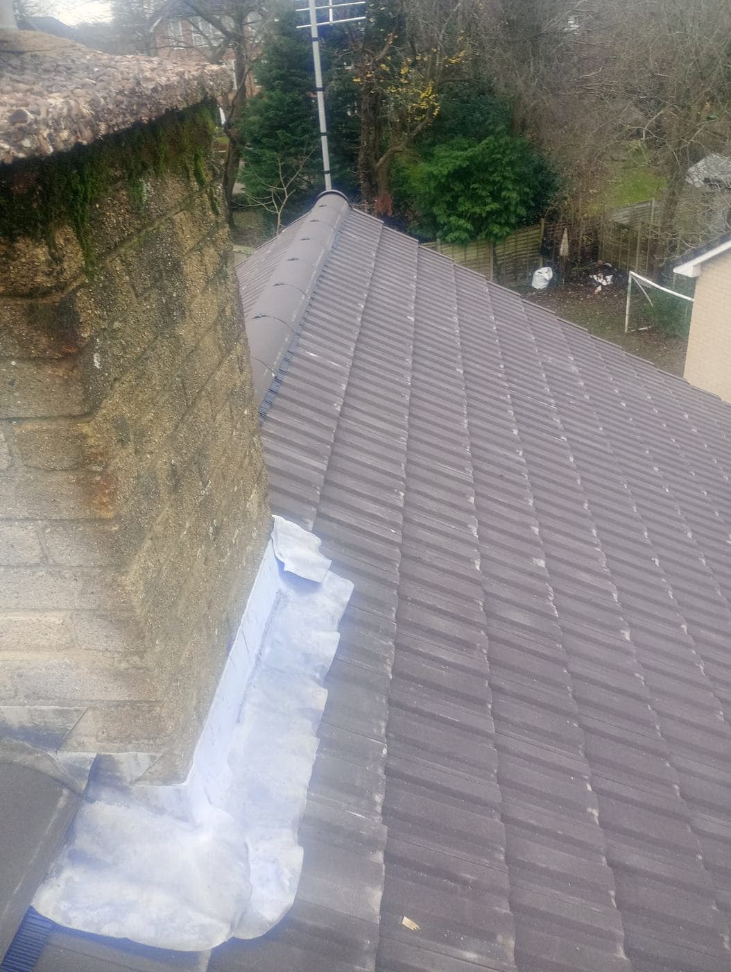 New flashing dressed against a mossy blockwork stack where the retiled slope meets it