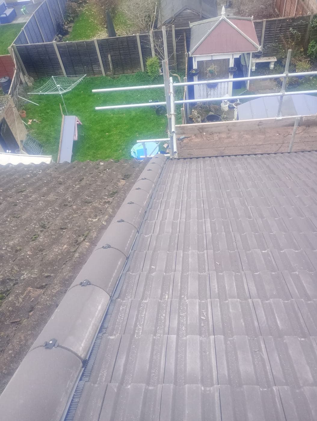 Clipped dry ridge separating new brown tiles from an old mossy slope, garden below