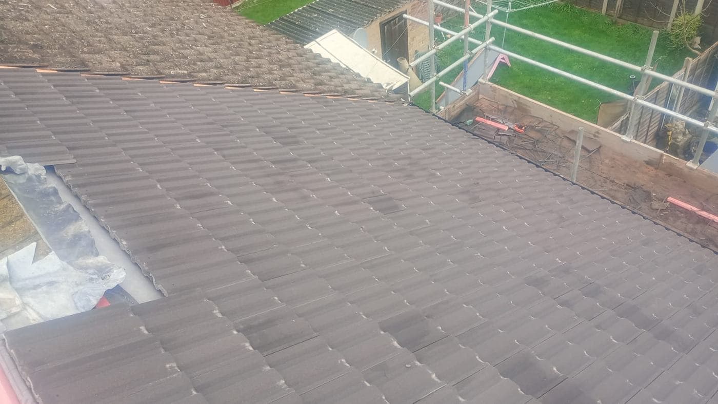 Newly laid dark grey-brown tiles running down to a lead valley, scaffolding and lawn beyond