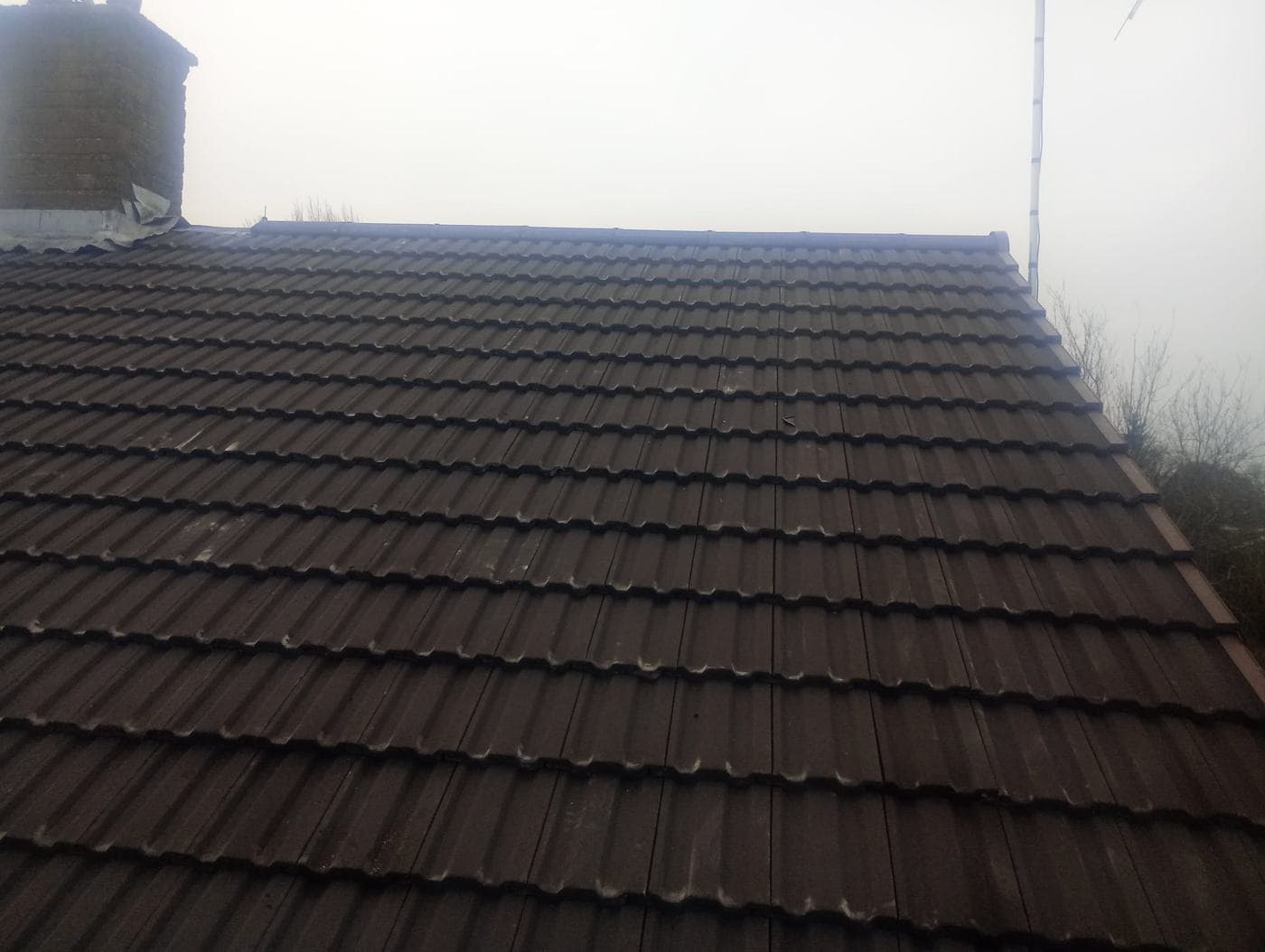 Dark brown tiled roof completed to the ridge in mist, weathered brick chimney at the gable