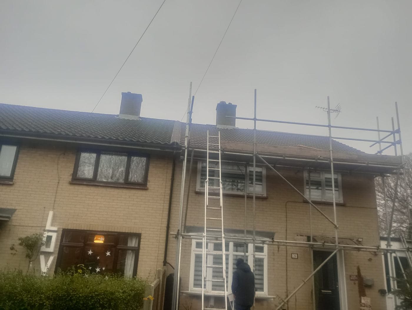 Scaffolded front of a terraced house in fading light, someone standing near the door