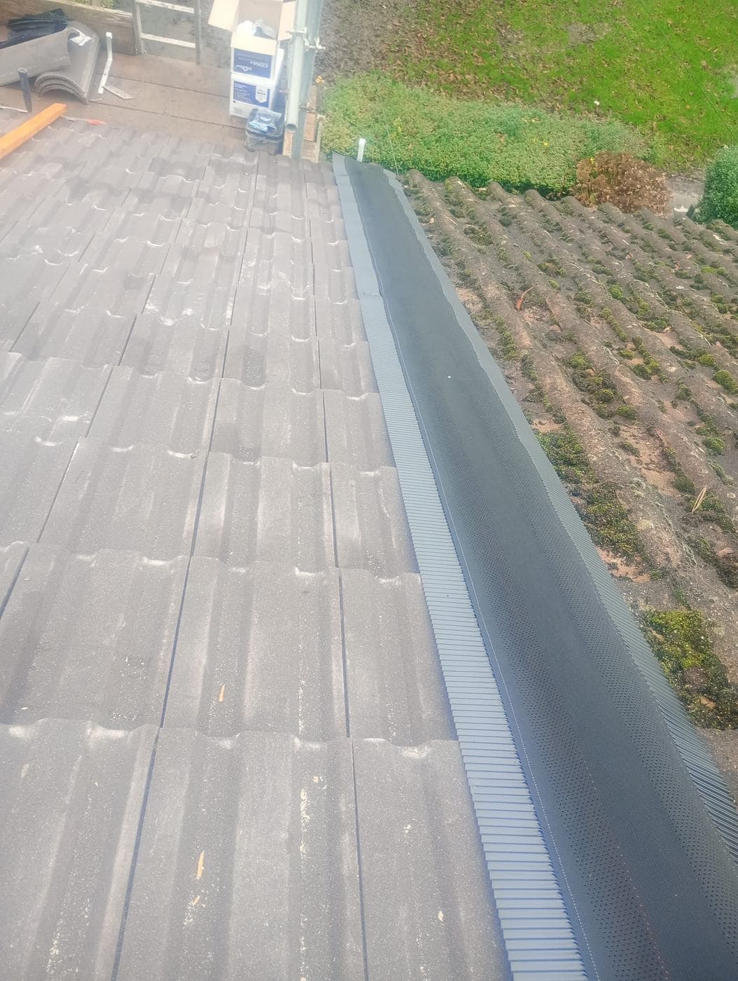 Grey perforated ridge roll laid along the ridge line, mossy neighbouring tiles beside it