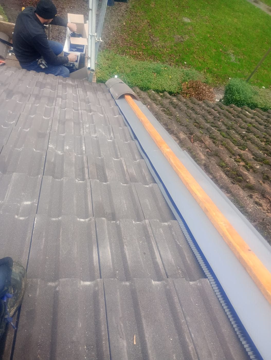 Roofer at the ridge opening a box of fixings beside a timber ridge batten