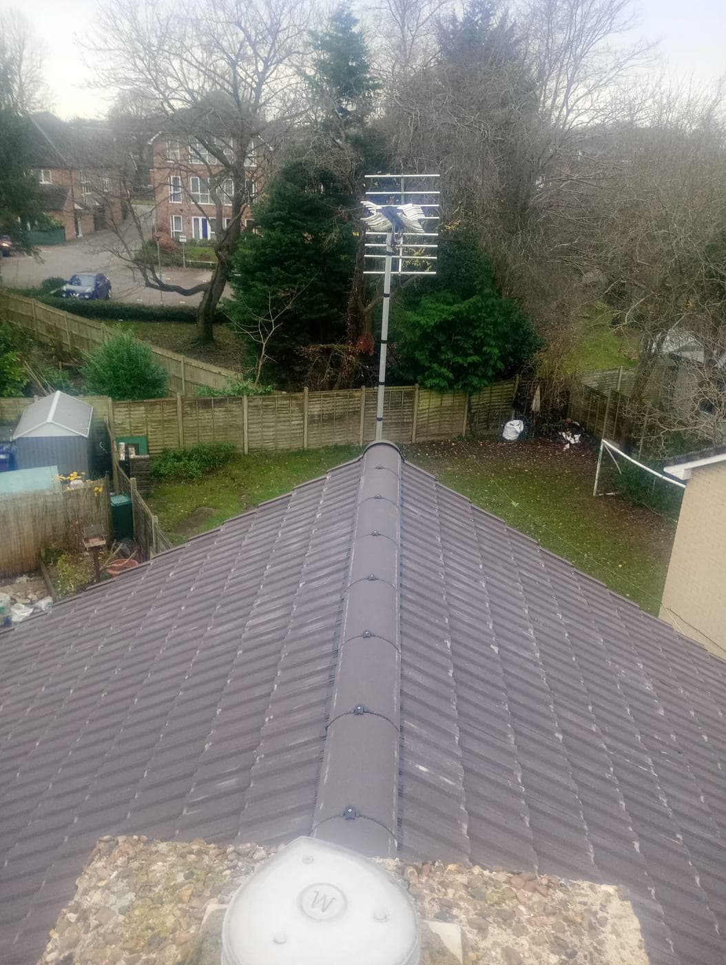Looking along a hipped roof ridge with fixed ridge tiles, back gardens and an aerial beyond