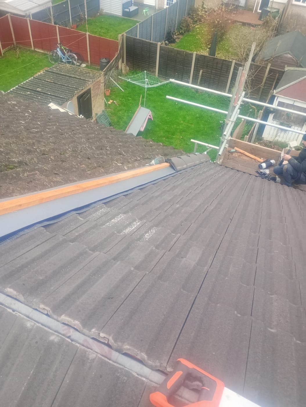 Newly laid grey concrete roof tiles beside fresh timber batten, back garden below