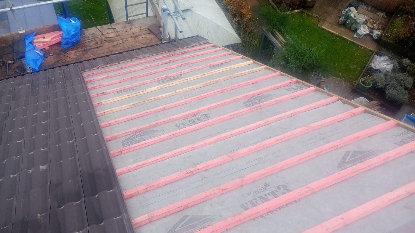 Breathable membrane and pink treated battens across half a roof, new tiles alongside