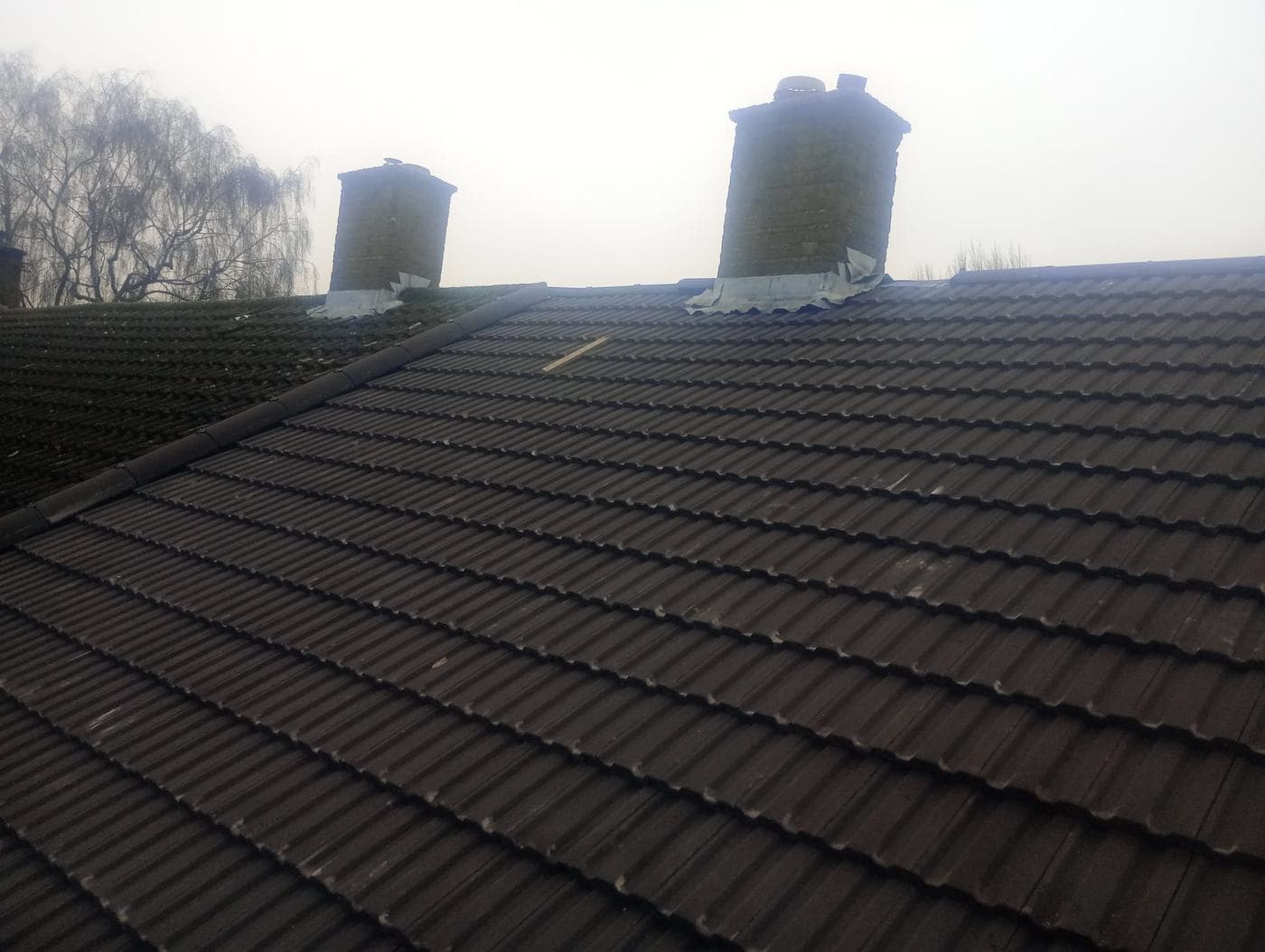 Two brick chimney stacks with fresh flashing rising from a dark tiled roof in mist