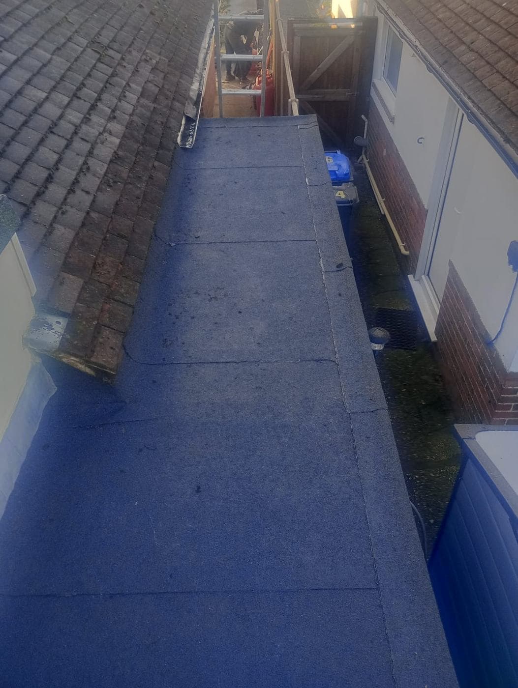 Finished grey felt flat roof running between a tiled pitch and a rendered bungalow wall