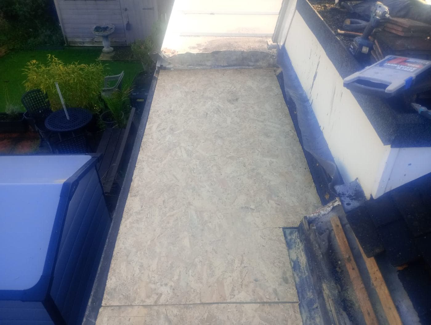 Fresh OSB boards decked across a narrow flat roof, tools resting on the trim