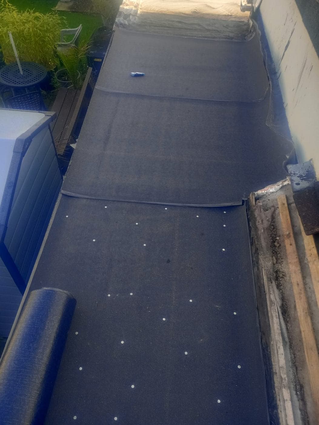 Felt underlay fixed with white capped nails, a fresh roll waiting at the edge