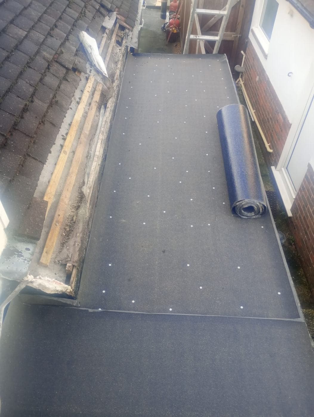 Felt underlay fixed with white discs, part-rolled felt beside stripped timber and old tiles