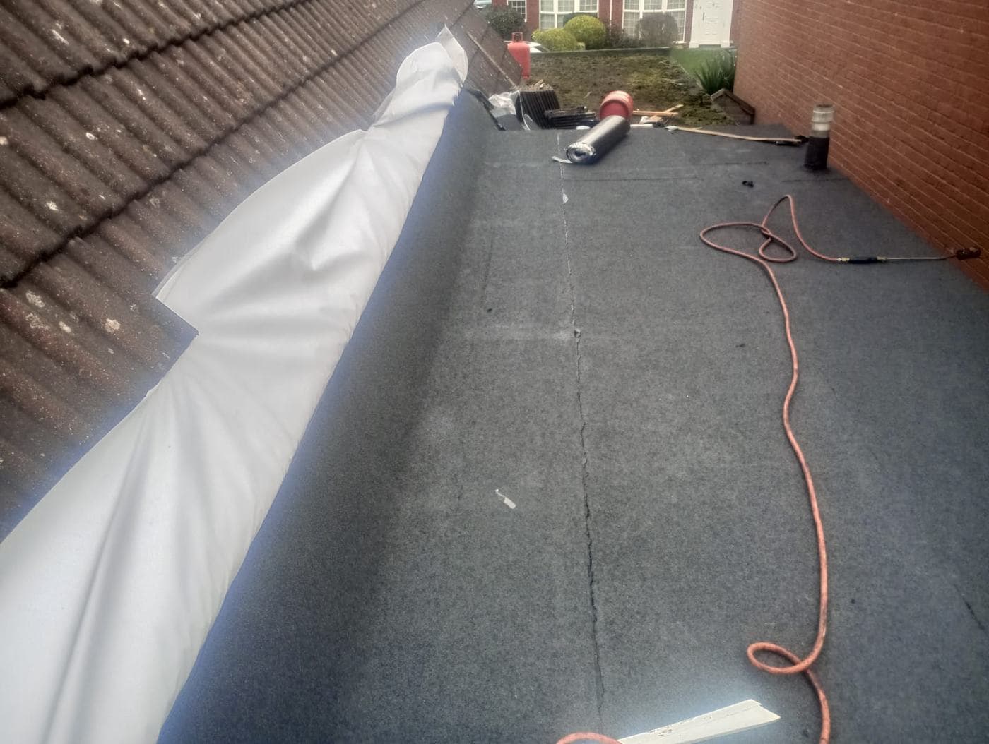 Sheeting rolled along the join where felt roofing meets the pitched tiled slope