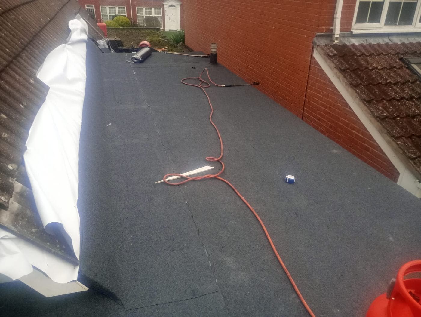 Felt roof between brickwork and tiles, torch hose, tape measure and roll of felt