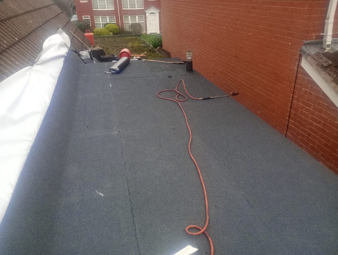 Long felt roof against a red brick flank wall, torch hose coiled across the surface