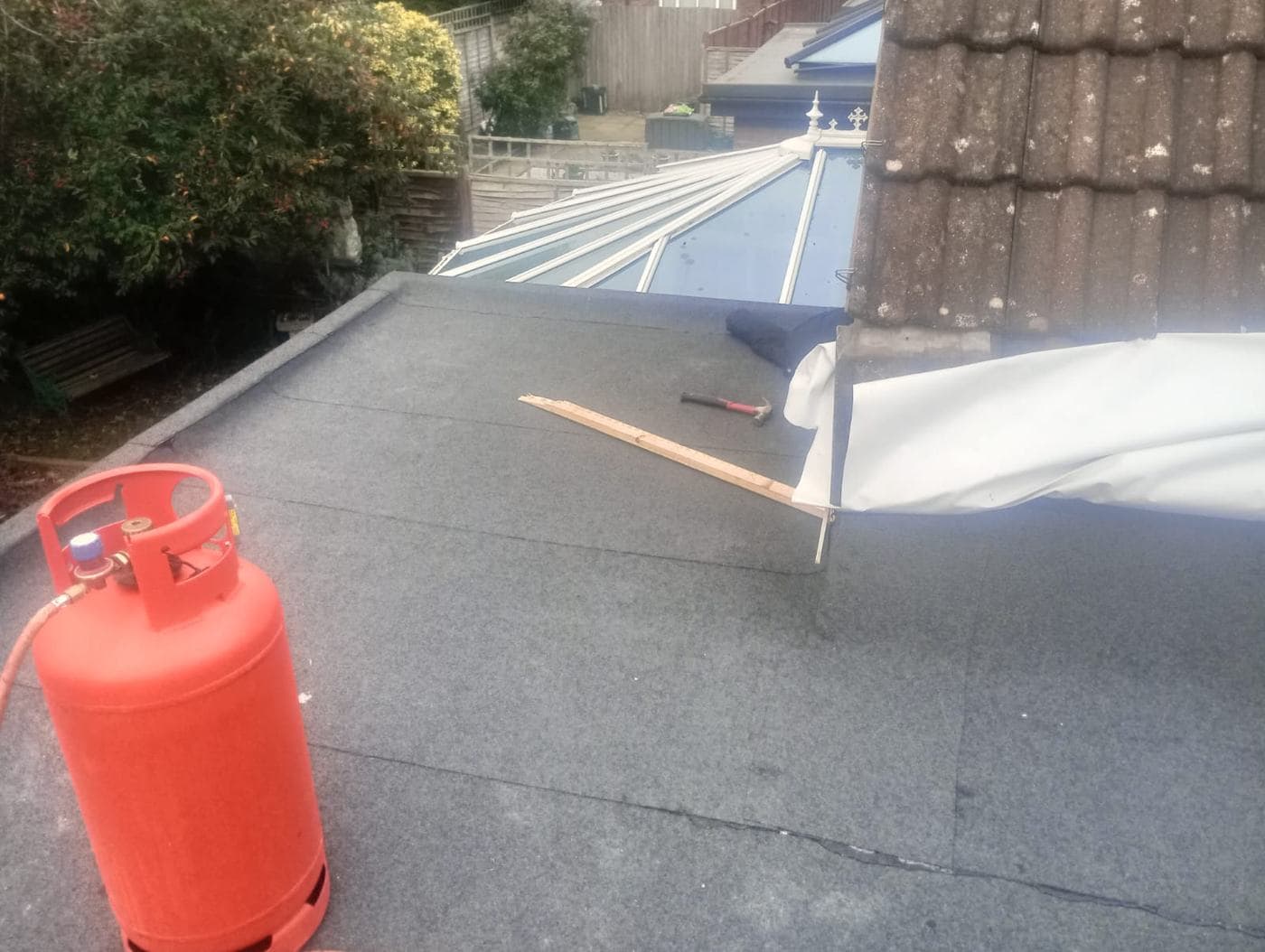 Grey felt roof running up to a white conservatory lantern, propane bottle and hammer alongside