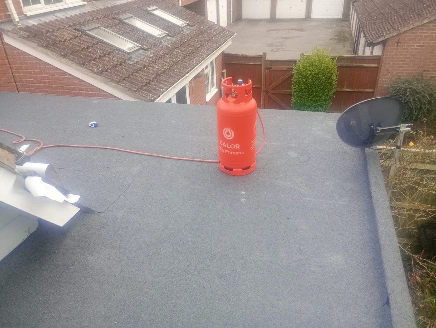 Red Calor propane cylinder and torch hose on felt, satellite dish at the roof edge